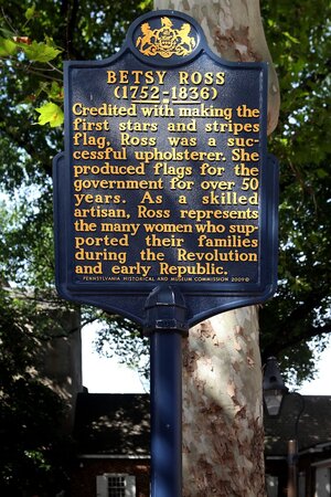 A navy metal signpost that reads 'BETSY ROSS (1752-1836)' followed by a few sentences in gold-colored paint A navy metal signpost that reads 'BETSY ROSS (1752-1836)' followed by a few sentences in gold-colored paint